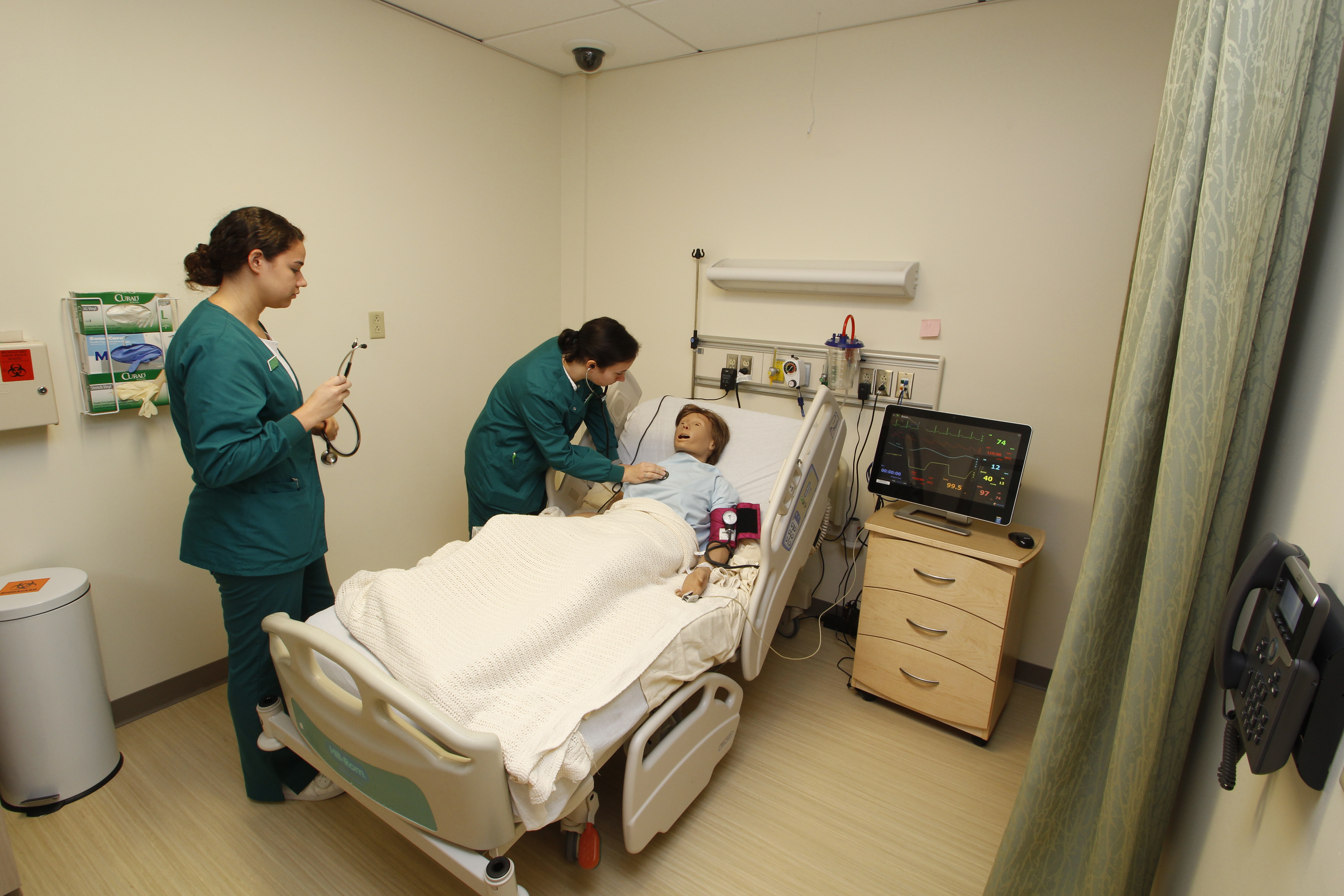 Two medical assistant students practice on a patient simulation